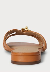 Šviesiai rudos odinės plokščiadangės šlepetės su suapvalintu nosimi, išpjautomis šoninėmis detalėmis ir auksiniu apvaliu akcentu ant dirželio. Sklandus paviršius ir žemas kulnas.