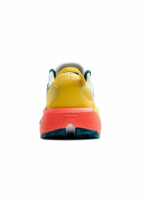 Zapatilla deportiva multicolor con parte superior de malla amarilla y blanca, acentos en azul verdoso y una suela de goma texturizada en rosa con un tacón prominente.