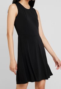 Musta ilmanhiha dressi kevyestä kankaasta, jossa on pyöreä pääntie ja liehuva hame, joka mahdollistaa liikkumisen vaivattomasti. Sileä tekstuuri, rento istuvuus.