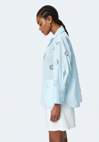 Himmelblaues Hemd mit floralen Ausschnittmustern,knöpfiger Front und langen Ärmeln. Kombiniert mit einem weißen Rock, der eine lockere Passform und eine weiche Textur aufweist.