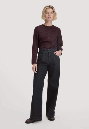 Dunkle hochtaillierte Jeans kombiniert mit einem burgunderfarbenen Langarmhemd mit Knopfleiste. Der Stoff wirkt glatt mit einem lässigen Schnitt und ohne sichtbare Muster.