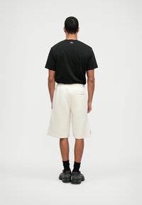 T-shirt en coton noir et shorts amples blancs avec taille élastique, dotés d'une poche arrière et d'échancrures sur l'ourlet.