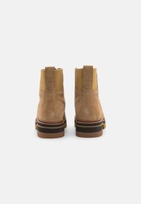 Botas tobilleras de ante marrón con un acabado texturizado, paneles laterales elásticos y una suela de goma apilada con rayas en contraste.
