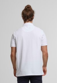 Polo bianco con colletto classico, maniche corte e una texture liscia. Presenta fessure laterali e dettagli di cucitura minimal.