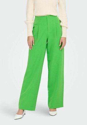 Pantaloni larghi verde con una texture liscia, vita alta, tasche laterali e chiusura con bottone frontale, abbinati a tacchi bianchi.