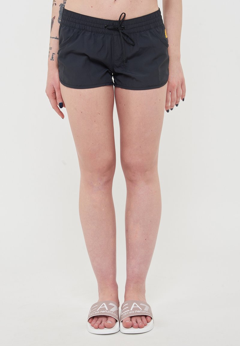 Pantaloni sportivi neri con vita elastica e lacci. Indossati con sandali bianchi a scivolo con logo.