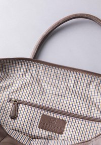 Brown leather handbag interior featuring a checkered fabric lining in beige, navy, and brown with a zip pocket and brand label.