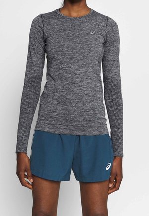 Personne portant un haut de sport gris ajusté à manches longues et un short ample bleu foncé avec un petit logo blanc sur chaque vêtement.