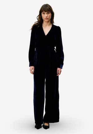 Marineblauw fluwelen jumpsuit met een V-hals, lange mouwen en een gestrikte taille. Wijde pijpen met een zachte textuur en subtiele glans.