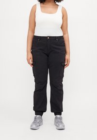 Svarta cargobyxor med sidofickor och elastiska muddar, tillsammans med en vit linne och grå sportskor. Slät tyg och skräddarsydd passform.