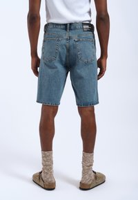 Shorts di denim, lavaggio blu chiaro con un classico design a cinque tasche. Vestibilità a vita media, sfilacciati all'orlo, indossati con calze spesse in maglia color marrone chiaro e pantofole.