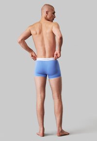 Boxer da uomo blu con una cintura elastica bianca che riporta il logo "Calvin Klein". Il design è aderente, con una texture liscia e un taglio corto.