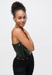 Camisolă din satin negru cu margini din dantelă, cu bretele subțiri și un design strâmt, asortată cu pantaloni negri cu talie înaltă.