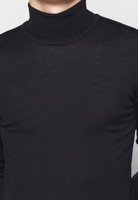 Maglione a collo alto nero realizzato in un tessuto a maglia liscio, con un design aderente e un logo discreto sul petto.
