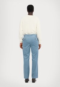 Blauwe corduroy broek met een ontspannen pasvorm, voorzien van een hoge taille en twee achterzakken met zwarte knopen. Gecombineerd met een lichte trui.