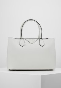 Sac en toile structuré blanc avec double poignées, présentant une surface texturée, des bords noirs contrastants et un accent de logo à l'avant.