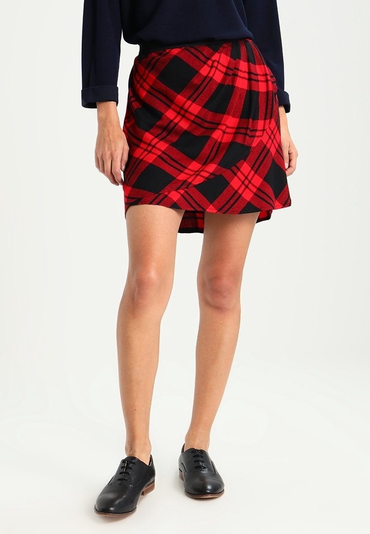 Punainen ja musta ruutuhame, joka on valmistettu pehmeästä kankaasta, ja siinä on kietaisumalli ja hieman levenevä helma, yhdistettynä mustiin kenkiin.