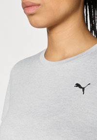 Tricou de bumbac gri cu guler rotund și mâneci scurte, având un mic logo negru cu o panteră săritoare în zona pieptului stâng.