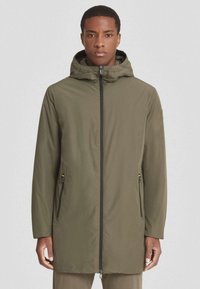 Chaqueta impermeable color verde oliva con capucha, cremallera negra y bolsillos laterales, con una textura suave y un diseño de corte relajado.