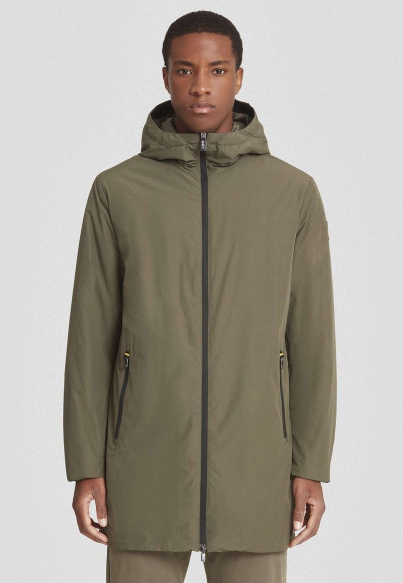 Chaqueta impermeable color verde oliva con capucha, cremallera negra y bolsillos laterales, con una textura suave y un diseño de corte relajado.