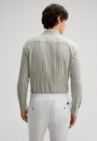 Hellgrünes kariertes Hemd aus strukturiertem Stoff. Mit klassischem Kragen und Knopfärmeln, kombiniert mit weißen Hosen.