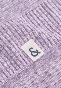 Helles lila gestricktes Kleidungsstück mit geripptem Muster und einem gewebten Etikett, das ein Und-Zeichen-Symbol zeigt. Nahaufnahme betont die Materialdetails.