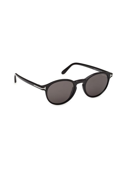 Lunettes de soleil rondes noires avec verres foncés et branches fines, ornées de petits logos "T" argentés près des charnières de chaque côté.