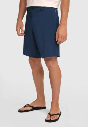 Pantaloncini blu navy realizzati in tessuto leggero, con chiusura a bottone, tasche laterali e taglio dritto, abbinati a infradito nere.