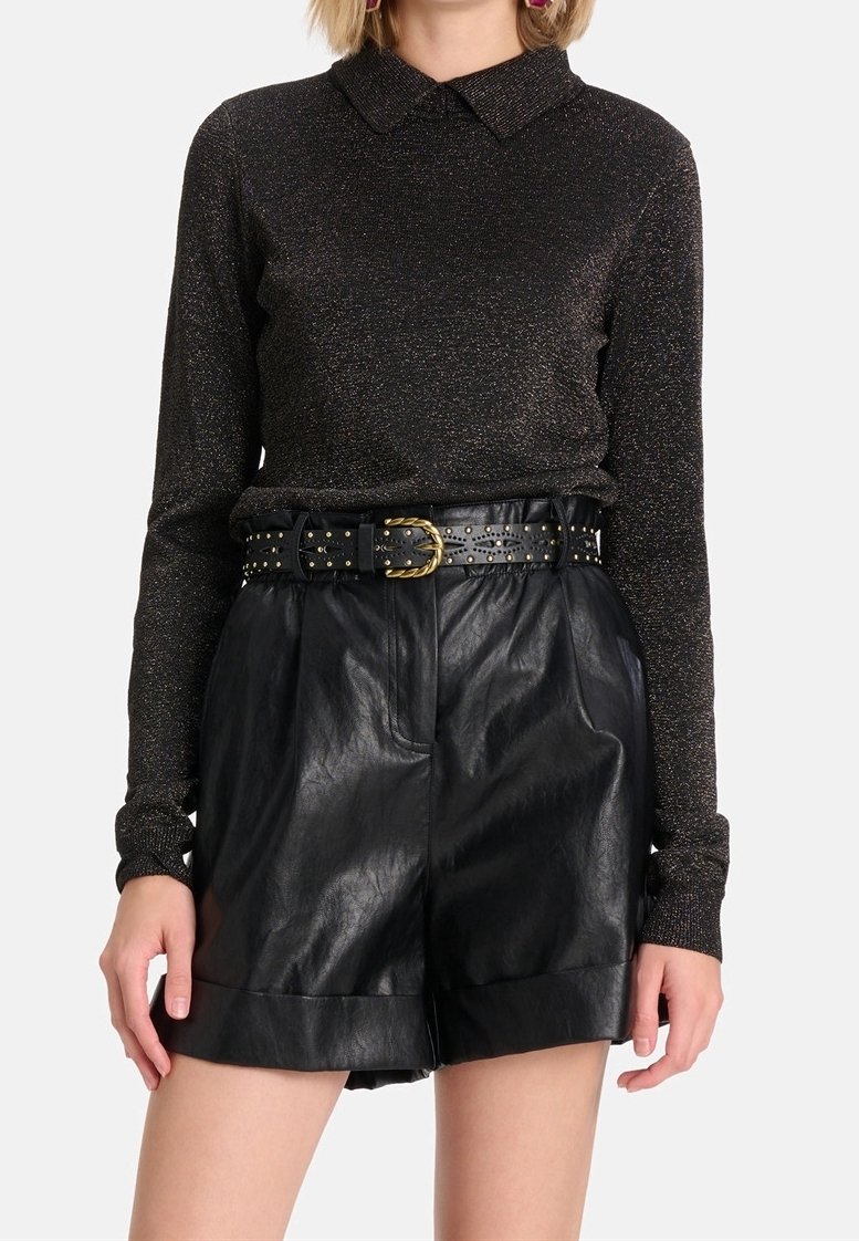 Haut noir à manches longues avec un col, présentant un léger scintillement, associé à un short en cuir noir taille haute et une ceinture noire cloutée.