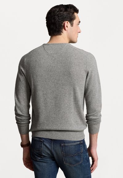 Grå strikket sweater med rund hals, ribbede manchetter og kant. Parret med blå denim jeans med baglommer med stikninger.