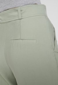 Ljusgröna byxor i slätt tyg, med en bakficka med platt öppning och en skräddarsydd passform runt midjan och höfterna.