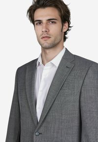 Grijze blazer met een gestructureerde afwerking, enkele knoopsluiting, notch revers en een wit overhemd eronder.