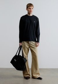 Črna majica z dolgimi rokavi, bež široke hlače in črna torba duffel z logotipom "BOSS"; gladke teksture in sproščen kroj.