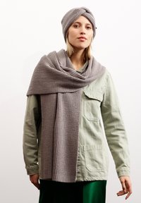 Grau gestricktes Mützen- und Schalset mit einem strukturierten Muster. Der Schal ist lang und hängt über einem hellgrünen Shirt, was einen grünen Rock ergänzt.