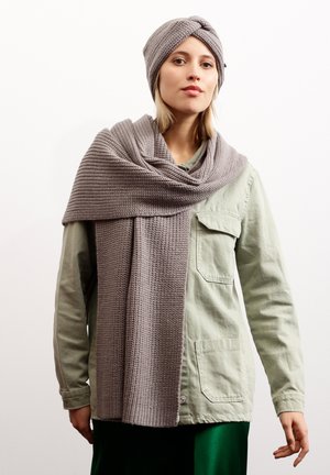 Set de bonnet et écharpe en tricot gris, avec un motif texturé. L'écharpe est longue et tombe sur une chemise vert clair, complétant une jupe verte.