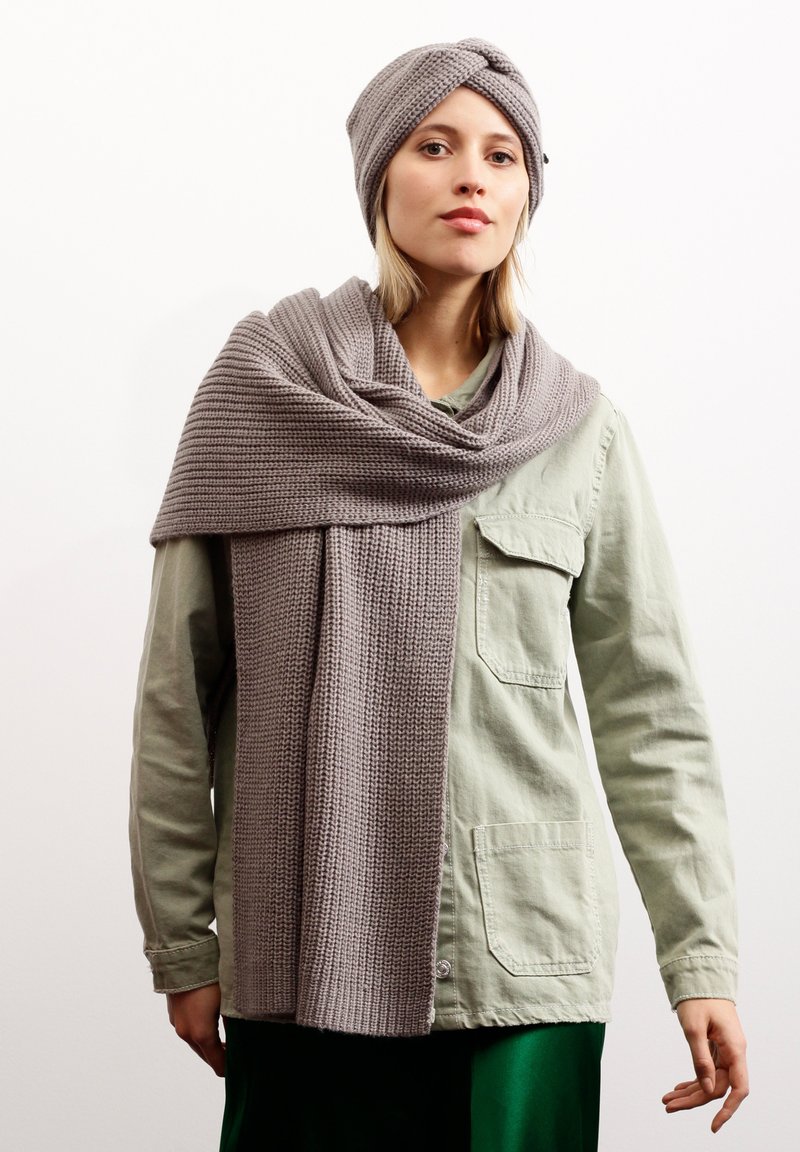 Grau gestricktes Mützen- und Schalset mit einem strukturierten Muster. Der Schal ist lang und hängt über einem hellgrünen Shirt, was einen grünen Rock ergänzt.