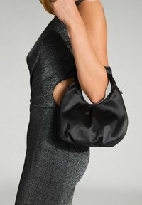 Borsa hobo in satin nero con un design morbido e arrotondato e una maniglia singola, tenuta da una figura che indossa un vestito nero scintillante.