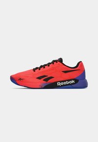 Shoe atlético vermelho brilhante com parte superior em malha texturizada, detalhes pretos, calcanhar roxo e sola de borracha com o logótipo da Reebok.