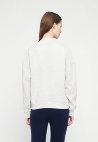 Hanorac gri deschis, cu croială lejeră, manșete și tiv striate, prezintă umeri căzuți și textură moale. Purtați cu colanți în nuanță navy.