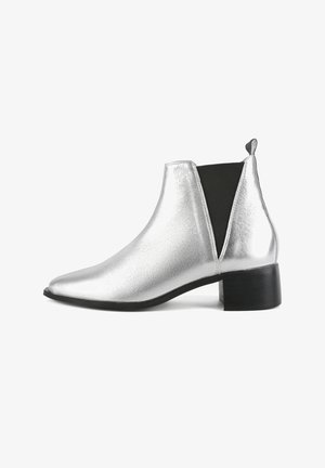 Srebrna metalik gležnjača s uskim nosom, elastičnim bočnim panama i niskim crnim blokom potplata. Glatka tekstura s sjajnim finišom.