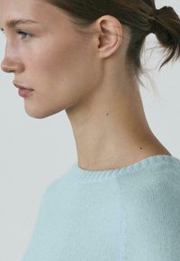 Maglione azzurro in maglia con collo rotondo, texture morbida e dettagli a coste sul colletto, visibile da un profilo laterale.