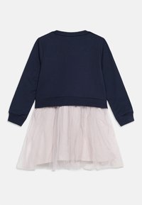 Μπλε ναυτικό τοπ με μακριά μανίκια που συνδέεται με ανοιχτό ροζ φόρεμα από τούλι με συστρεφόμενα στρώματα, εμφανιζόμενο από πίσω σε λευκό φόντο.