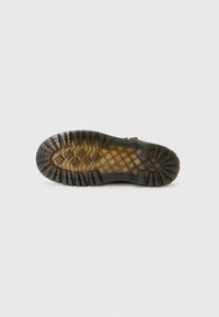 Outdoor shoe sole features a textured black rubber with a tan midsole, showcasing a tread pattern for traction and durability.
