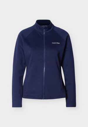 Tumši zila pilna rāvējslēdzēja jaka ar stāvošu apkakli, garām piedurknēm, sānu kabatām un Calvin Klein logotipu augšējā kreisajā krūšu daļā.