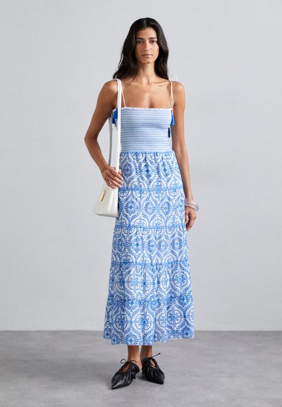 Sininen ja valkoinen kuviollinen maxi-mekko, jossa on kuminauhalla varustettu yläosa, säädettävät olkaimet ja kerroksellinen hameosa. Yhdistetty mustiin kenkiin ja valkoiseen laukkuun.