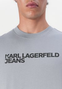 Pelēks kokvilnas T-krekls ar apaļu kakla izgriezumu un uzrakstu melnā krāsā "KARL LAGERFELD JEANS" uz priekšpuses. Gluda tekstūra.