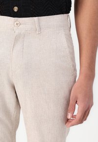 Beige Leinenhose mit strukturiertem Oberflächen, reguläre Passform, zwei Seitentaschen und Knopfverschluss am Bund.