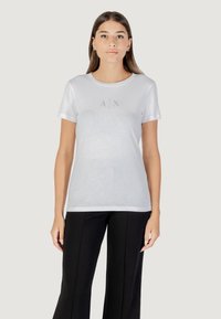 Bijela kratkotrajna majica s kratkim rukavima, okruglog izreza, na kojoj se nalazi logo "A|X ARMANI EXCHANGE" u srebrnom tekstu preko prsa. Glatka tekstura.
