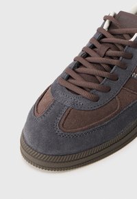 Brązowe i szare zamszowe trampki z teksturowaną cholewką, okrągłym noskiem i płaskimi sznurowadłami, z gumową podeszwą i szytymi detalami.