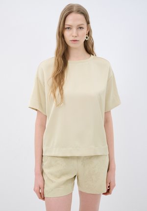 Beige kortærmet top med rund halsudskæring, glat tekstur og afslappet pasform, parret med lysebeige mønstrede shorts.